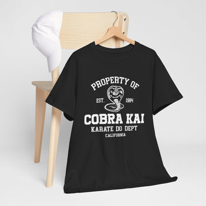 Sophisticated black T-shirt bearing the Cobra Kai logo, placed on a wooden chair next to a white cap, exemplifying a trendy casual outfit for fans.