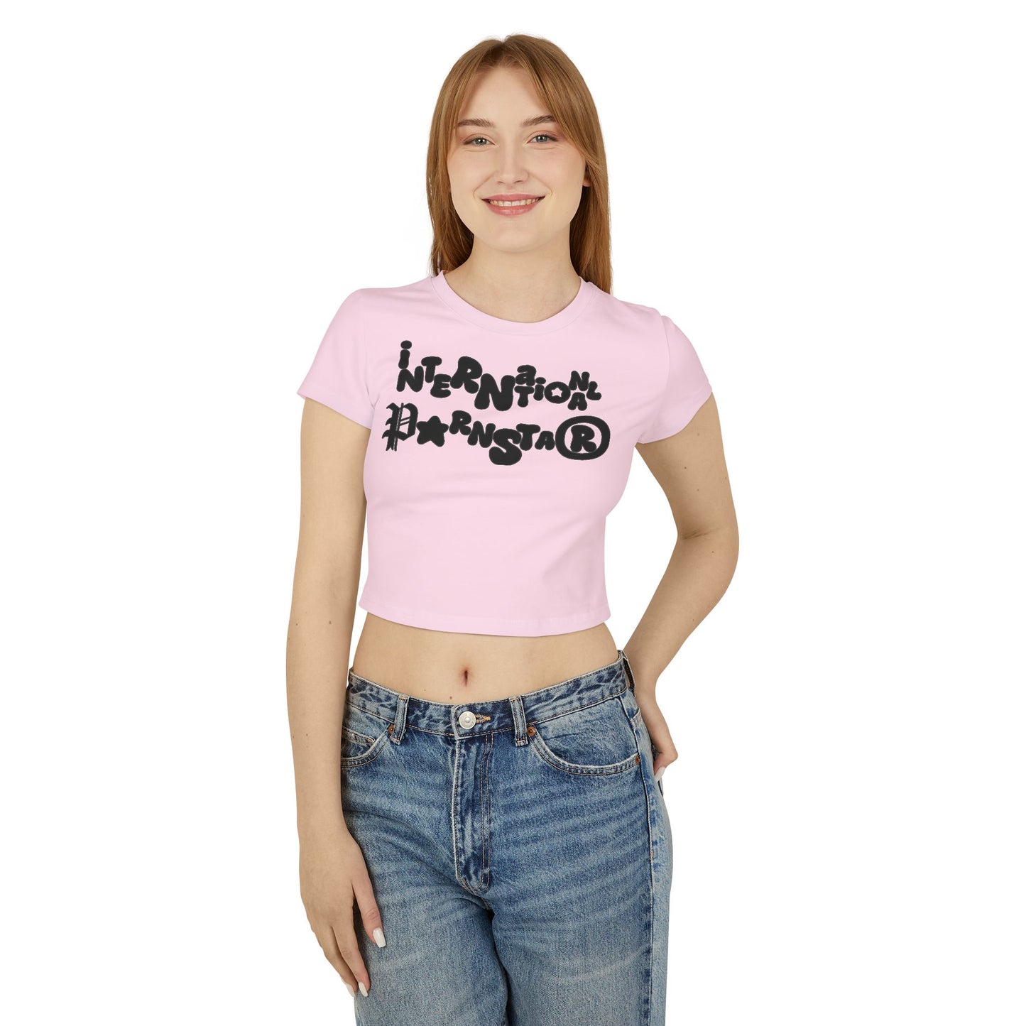 Fashionable model wearing a chic pink cropped baby T-shirt with 'INTERNATIONAL PARNSTAR' graphic, paired with high-waisted jeans, exemplifying playful luxury in casual wear.