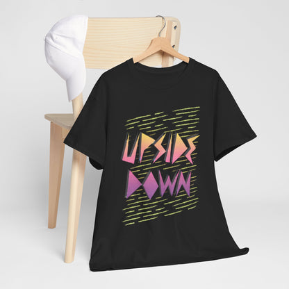 Chic black T-shirt with a striking 'UPSIDE DOWN' graphic, casually draped over a minimalist wooden chair, paired with a stylish white cap.