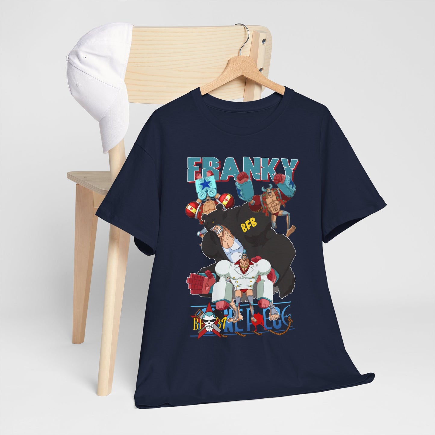 Stylish navy blue t-shirt with vibrant anime graphic, 'FRANKY', displayed alongside a chic white cap on a wooden chair, embodying modern fashion in a serene environment.