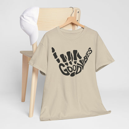 Stylish unisex t-shirt with a printed 'Good Vibes' skeletal hand gesture, casually styled with a cap on an elegant wooden chair, perfect for urban outings.