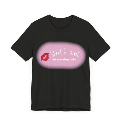 Front view of a stylish black unisex tee featuring an eye-catching vibrant lipstick print with the phrase 'Short 'n sweet, I'm working late...' inspired by Sabrina Carpenter.