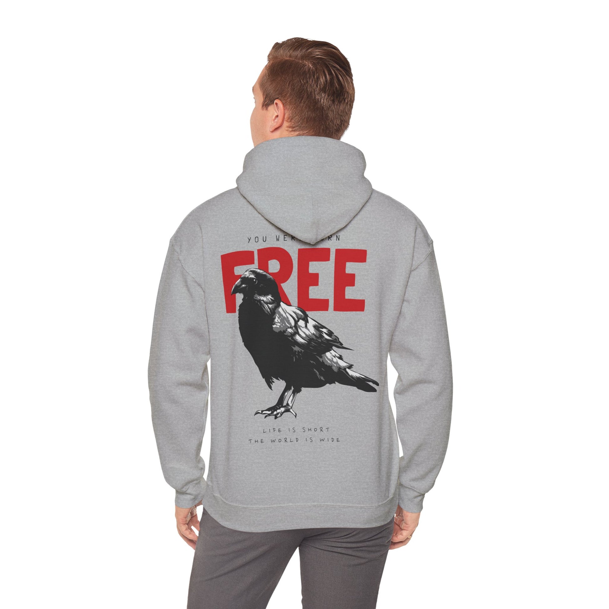 Man wearing a luxurious grey hoodie with a raven graphic on the back, displaying the statement 'YOU WERE BORN FREE' in striking red, paired with a relaxed yet sophisticated look.