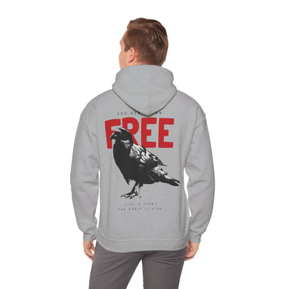 Man wearing a luxurious grey hoodie with a raven graphic on the back, displaying the statement 'YOU WERE BORN FREE' in striking red, paired with a relaxed yet sophisticated look.