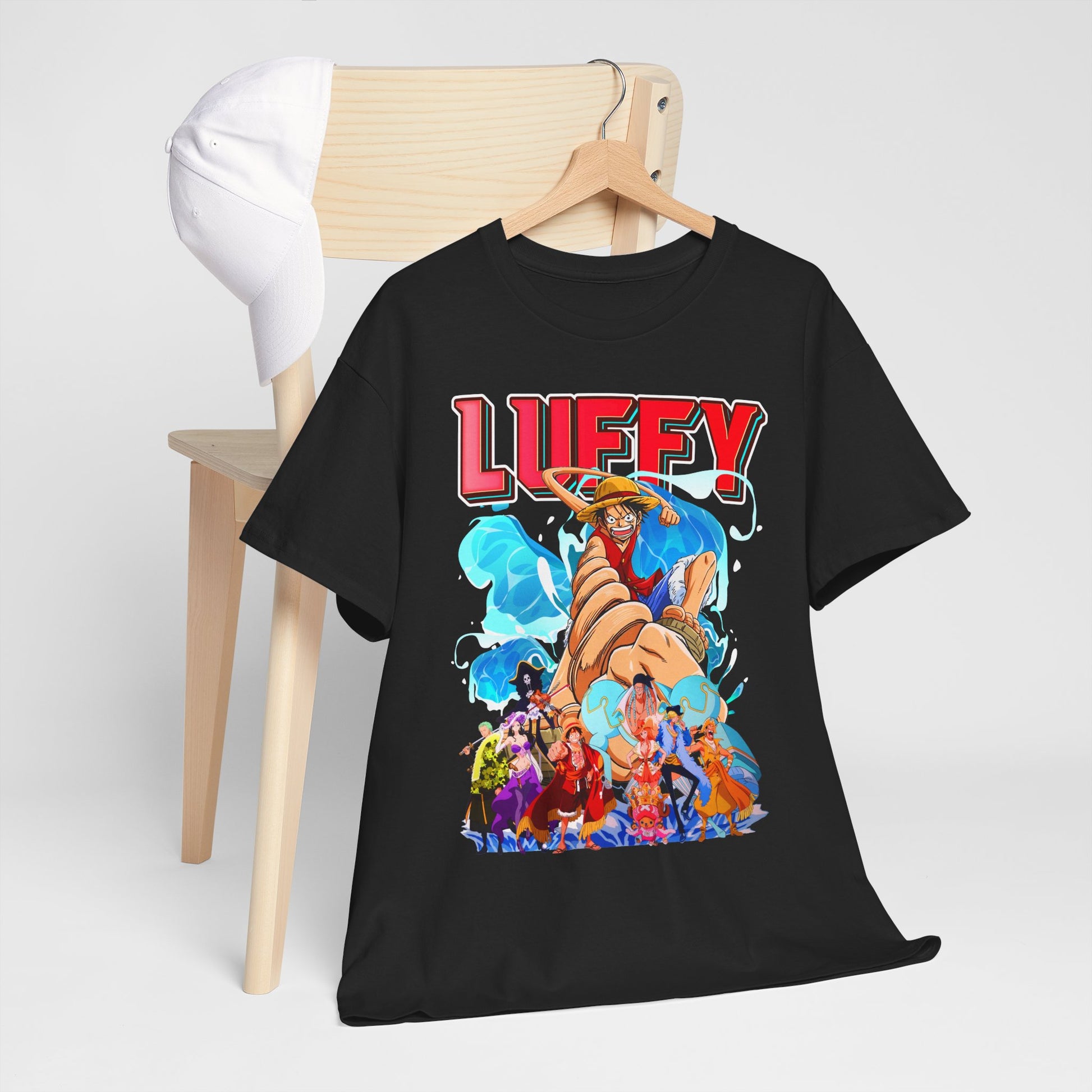 Luxurious black graphic t-shirt featuring a vibrant print of Luffy, complete with playful characters from an anime adventure, elegantly displayed on a wooden hanger beside a stylish cap.
