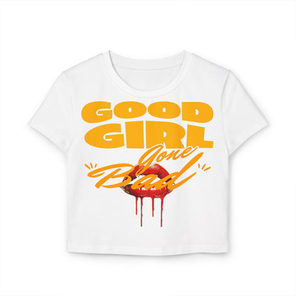 Luxurious white crop tee featuring bold ‘Good Girl Gone Bad’ design with vibrant orange-yellow lettering and striking red lips graphic, perfect for playful elegance.
