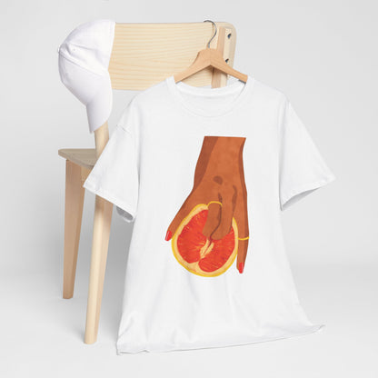 Vibrant Grapefruit Women's Graphic T-Shirt styled with a hat on a chic wooden chair, highlighting the artistic representation of a hand holding a grapefruit, an embodiment of luxury and modern elegance.