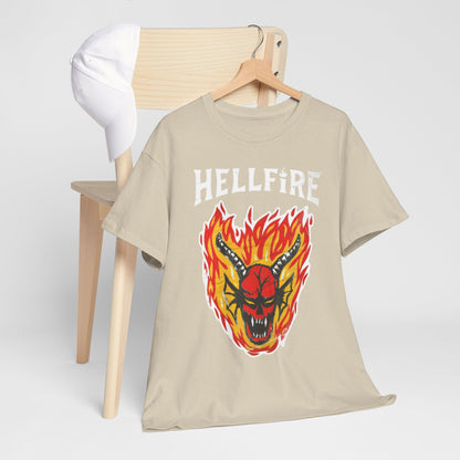 Luxurious beige Hellfire Club graphic t-shirt featuring a striking demon head design engulfed in flames, elegantly displayed on a minimalist wooden chair next to a white cap.