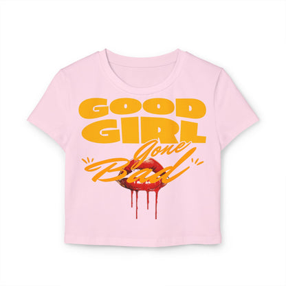 Close-up of a luxurious cropped Baby T-shirt in soft pink, adorned with a bold 'Good Girl Gone Bad' graphic and luscious red lips, blending cheekiness with refined style.