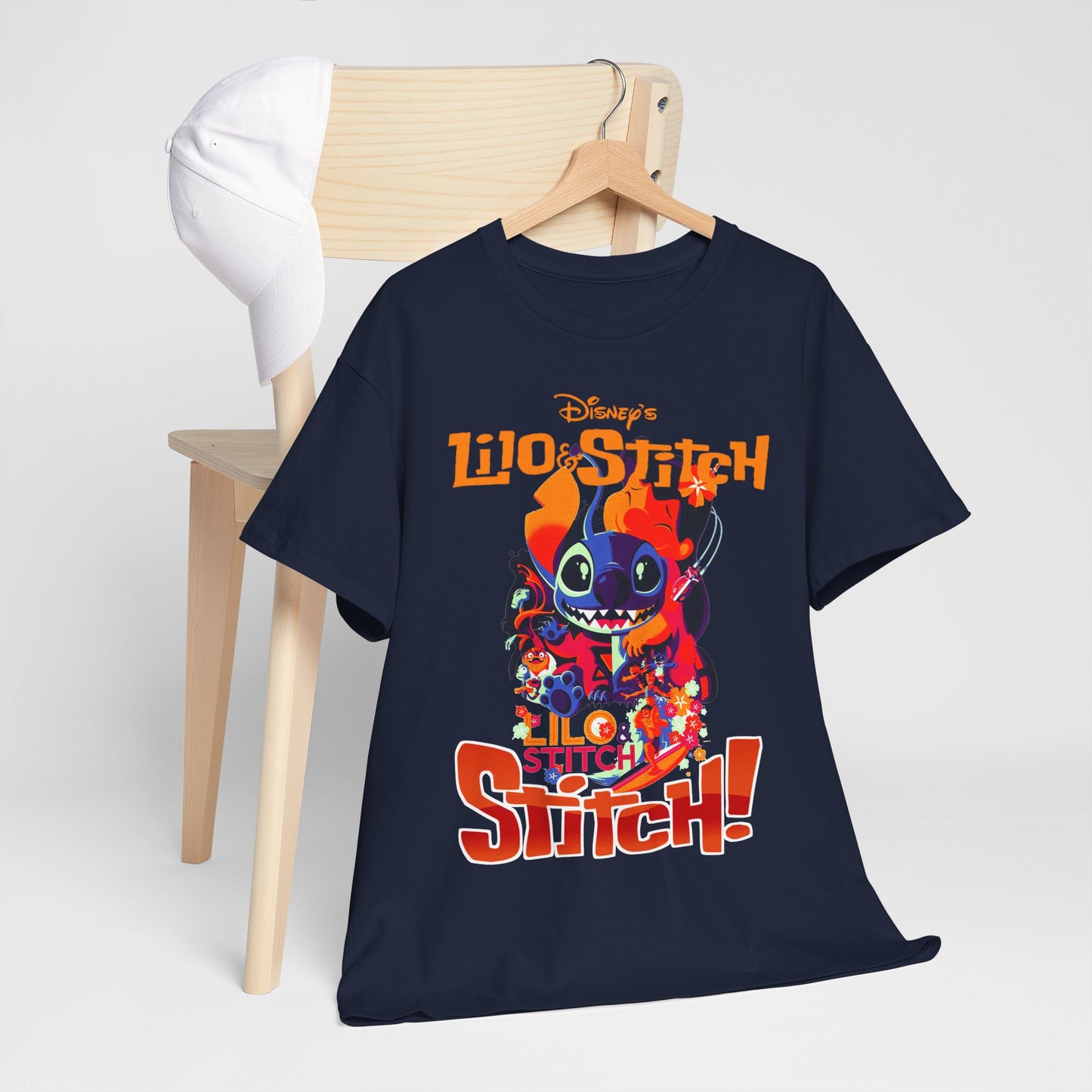 Sophisticated presentation of a navy blue Lilo & Stitch graphic t-shirt draped over a wooden chair alongside a white cap, combining luxury and charm for Disney fans.