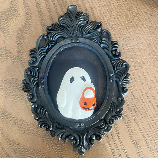 Elegant Halloween Resin Ornament - Trick or Treat Ghost Wall Decoration. A charming white ghost with a pumpkin basket adorns a decorative black frame, enhancing Halloween décor.