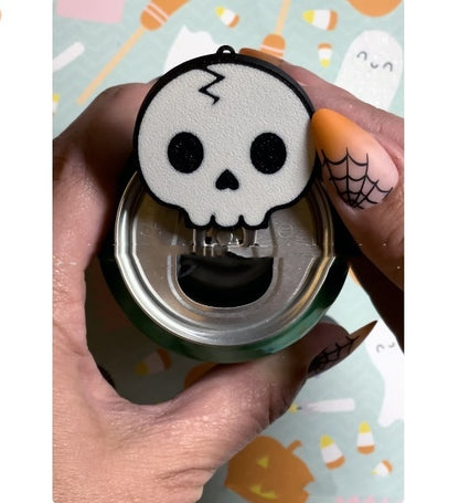 Chic skull design soda can tab opener held above a green can, featuring a keychain strap, showcasing functional elegance for drink aficionados.