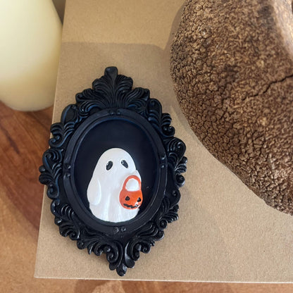 Halloween Resin Ornaments Trick Or Treat Ghost Wall Decoration featuring an adorable ghost holding a pumpkin basket, elegantly framed in a chic black ornate frame, perfect for upscale Halloween décor.