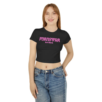 A smiling model in a luxurious black cropped t-shirt, featuring striking pink text 'PORNSTAR' and 'It's A Secret', blending humour with high-end fashion.