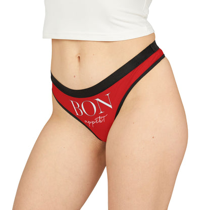 Luxurious women's thong featuring the whimsical phrase 'BON appétit' in elegant typography, designed for playful intimacy. The garment showcases a vibrant red fabric with stylish black trim, ideal for cheeky occasions and enhancing romantic moments.