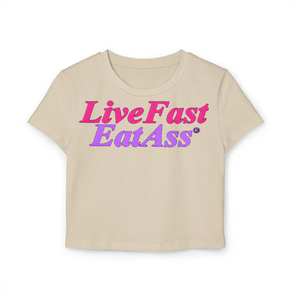 Luxurious cropped t-shirt featuring the playful slogan 'Live Fast Eat Ass' in vibrant hot pink and purple gradient design, crafted from 100% organic cotton.
