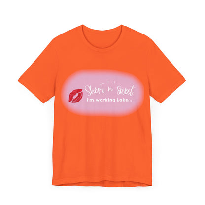 Front view of the bright orange Sabrina Carpenter Inspired Unisex Short Sleeve Tee featuring the playful text 'Short 'n' sweet, I'm working late...' with a vibrant lipstick accent.