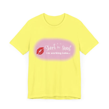 Front view of a vibrant yellow unisex tee displaying a playful lipstick print with the phrase 'Short 'n sweet, I'm working late...' inspired by Sabrina Carpenter.
