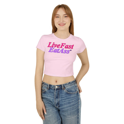 Front view of a fashionable cropped T-shirt in soft pastel pink, featuring the attention-grabbing slogan 'Live Fast Eat Ass®' in bold purple and pink, modelled by an elegant woman.