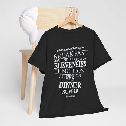 Luxurious black graphic tee featuring whimsical Hobbits' meal schedule, styled against a minimalist backdrop with a wooden chair and cap, ideal for urban streetwear.
