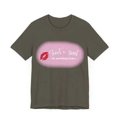 Sabrina Carpenter Inspired Unisex Short Sleeve Tee featuring a vibrant lipstick print, elegantly styled with the phrase ‘Short ‘n’ sweet, I’m working late’ in luxurious font.