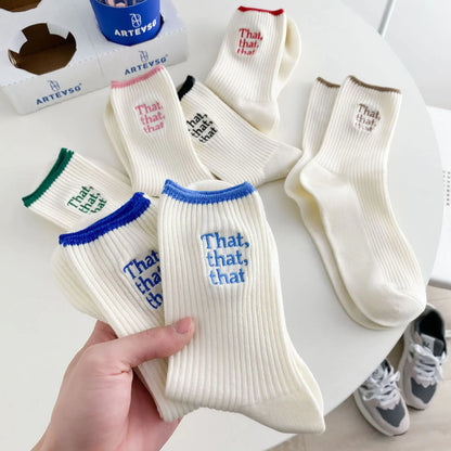 A collection of elegant white embroidered socks for women, featuring a unique Japanese-style font design. The socks are displayed in a stylish arrangement, showcasing varying colours of embroidered text, including blue, green, red, and black on a soft ivory background, perfect for elevating your fashionable attire.