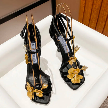 Elegant black high heel sandals featuring a gold flower metal strap, designed for parties and formal occasions, combining sophistication and style.