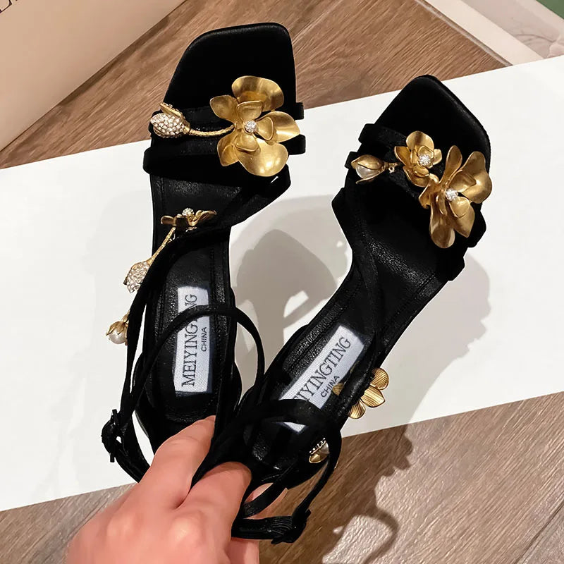Stylish profile view of black high heel sandals with intricate gold flower detailing, perfect for adding a touch of elegance to any formal wear.