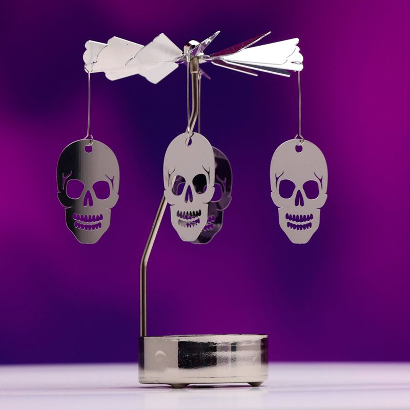 Gothic Spinning Skulls Tea Light Candle Holder in elegant metal design, showcasing 12cm height, casting intricate shadows from a tealight candle, perfect for gothic home decor.