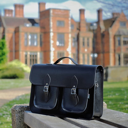 Luxury black twin pocket leather satchel handcrafted in England, designed for 13-16 inch laptops, showcasing elegance and functionality with dual front pockets and a detachable shoulder strap.