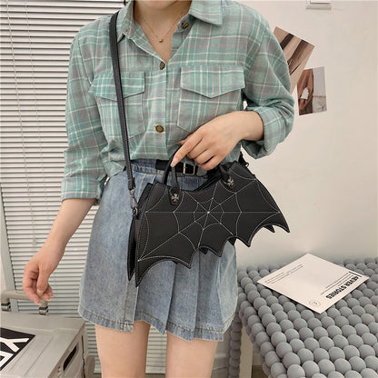 Stylish young woman holding a black Halloween Spider Web Shape Shoulder Bag with a unique bat design, perfect for enhancing seasonal outfits with a luxe touch.