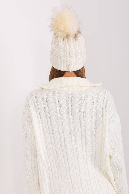 Elegant Rue Paris winter beanie for women, highlighting a sophisticated turn-up design with decorative plaid weave and fluffy pom-pom, composed of 70% acrylic and 30% wool.