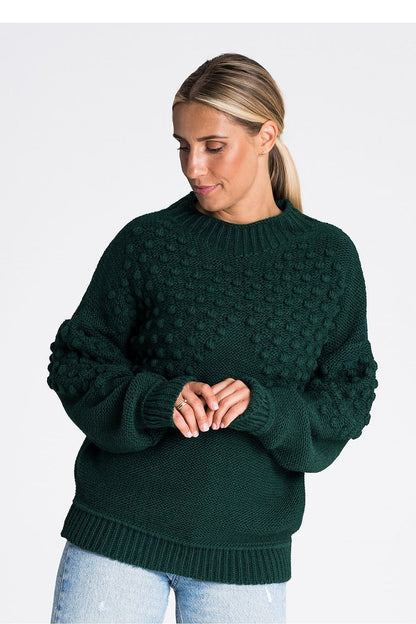 Figl’s elegant long sleeve sweater draped elegantly, showing off its structured ribbed edges and playful pom-poms, ideal for enhancing chic winter outfits.