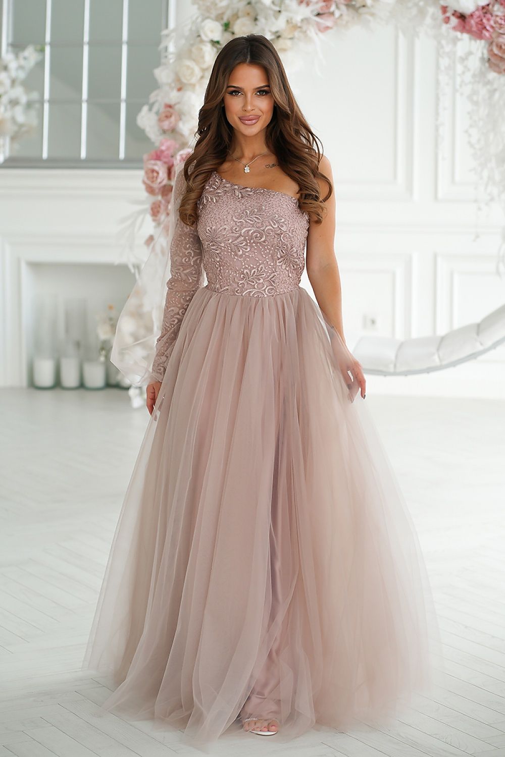 Stunning elegant one shoulder prom dress by Bicotone, featuring intricate shimmering lace and a flared mesh skirt in a soft pink hue, showcased in a beautifully lit interior.