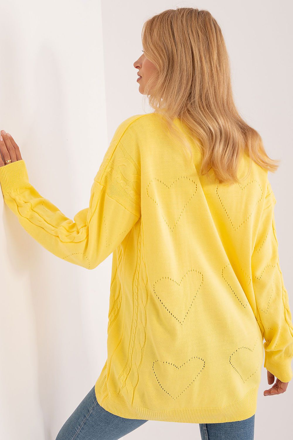 Stylish Badu yellow cardigan with heart motifs, elegantly posed against a wall, highlighting its sophisticated design.
