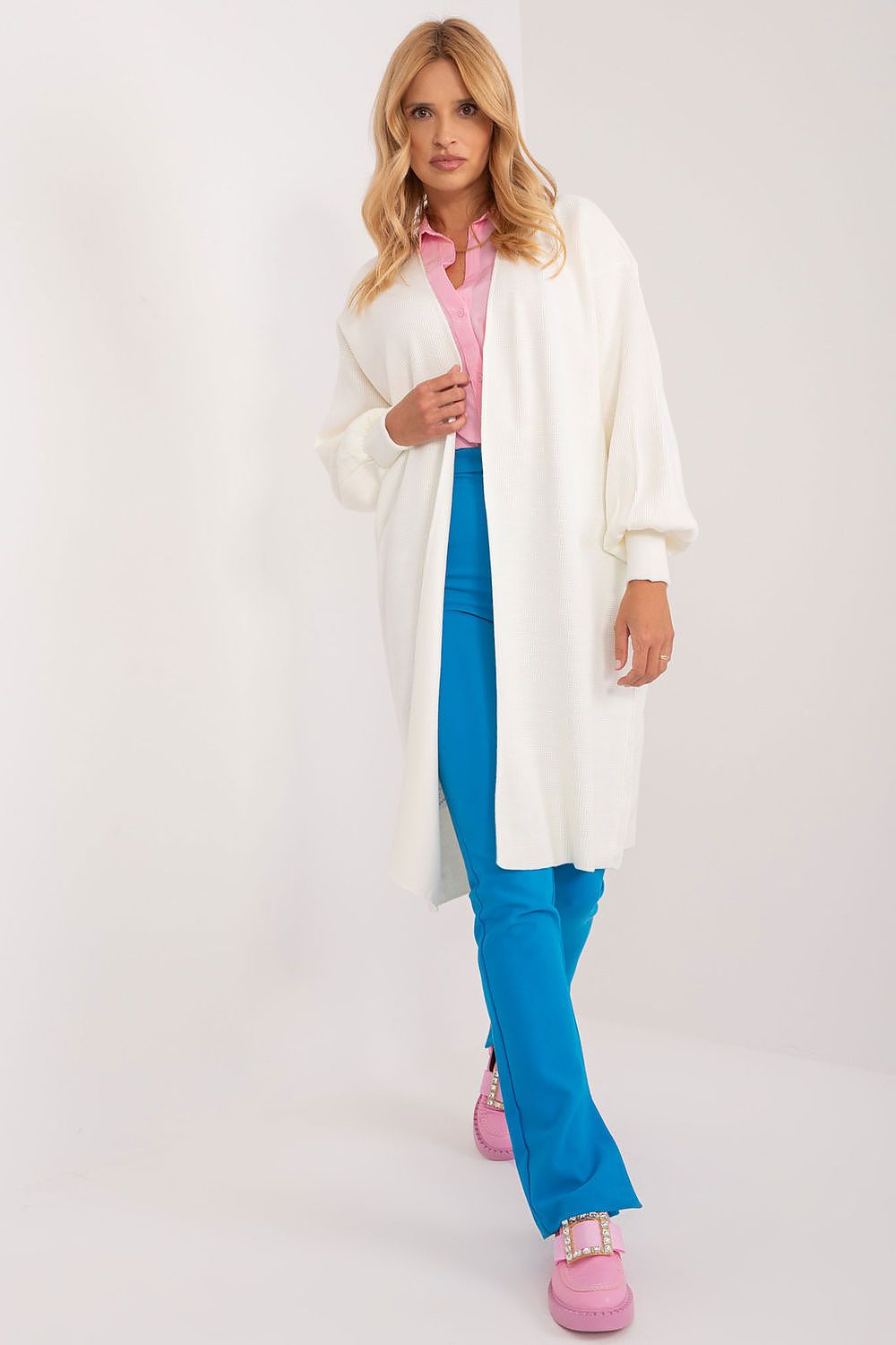 Model showcasing an elegant unbuttoned cardigan from Badu in a soft acrylic and wool blend, styled with vibrant blue trousers and pastel pink footwear for a chic, luxurious look.