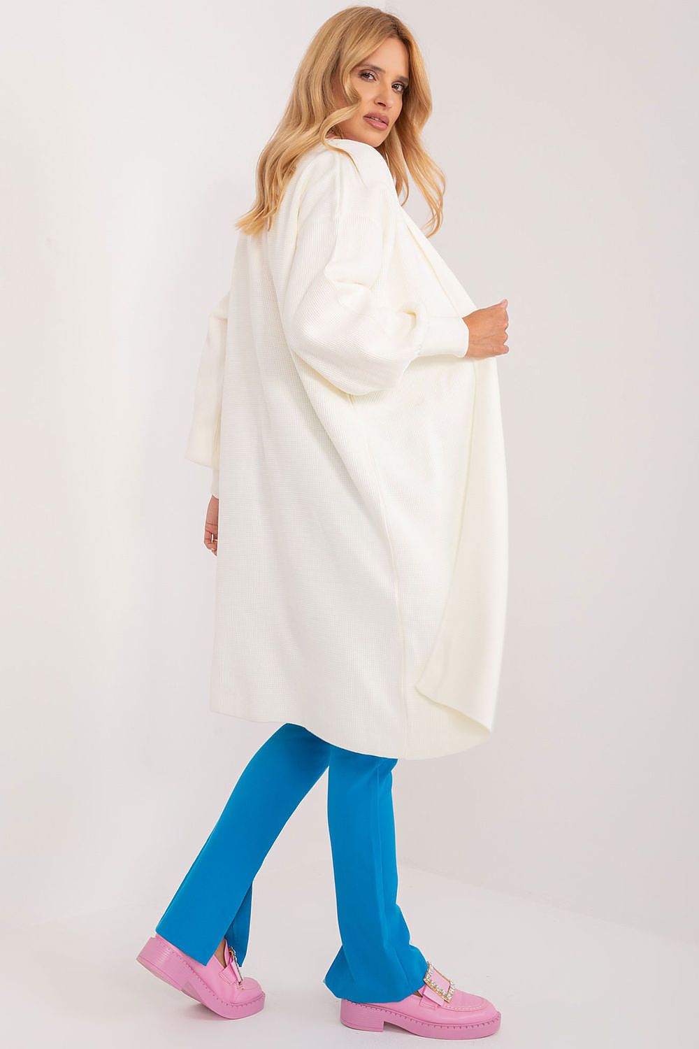 Side view of a model in an elegant unbuttoned cardigan by Badu, featuring a flowing silhouette paired with blue trousers, highlighting the stylish and versatile design.