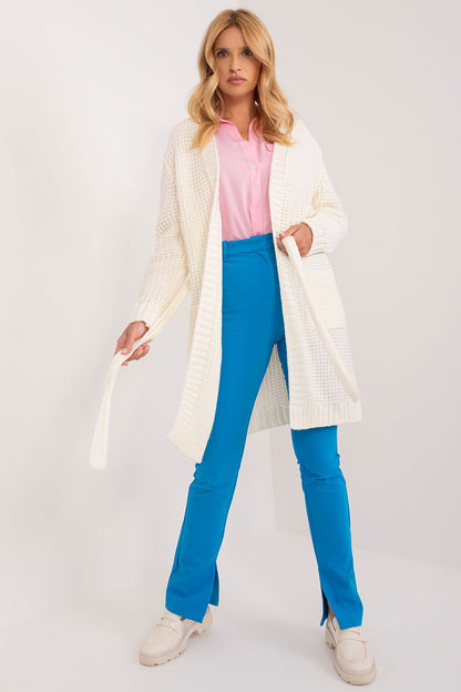Stylish woman wearing an elegant unbuttoned cardigan with a tie belt from Badu, featuring a sophisticated long length design, paired with vibrant blue trousers and a pink blouse, perfect for a luxurious everyday look.