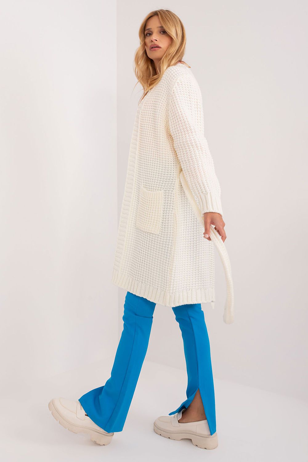 Elegant unbuttoned cardigan with tie belt by Badu, worn casually by a model in light colours, showcasing its stylish long length and textured fabric.