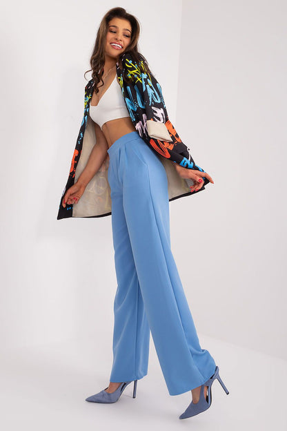 Stylish model in a fashionable ensemble featuring blue high waist trousers and an artistic jacket, representing luxury and modern flair by Rue Paris.