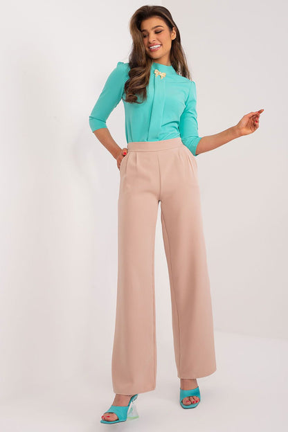 Chic model showcasing high waist tailored trousers by Rue Paris, complemented by a vibrant turquoise blouse and fashionable heels, exuding sophistication and poise.