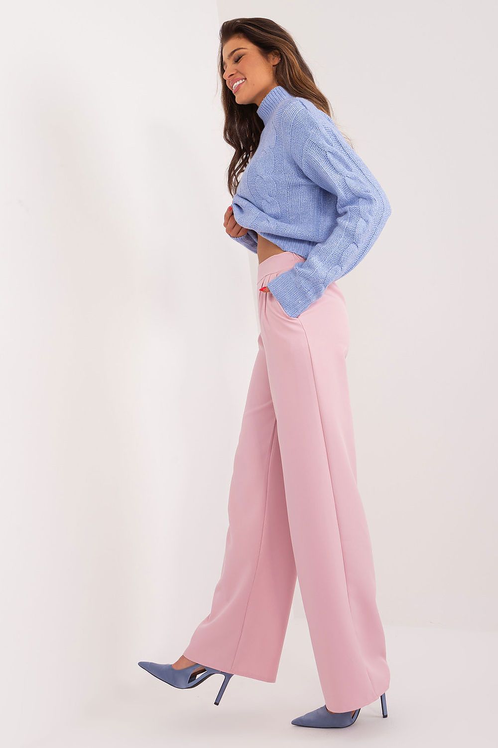 Side profile of an elegant woman wearing tailored pink trousers paired with a blue cropped sweater, exuding modern sophistication by Rue Paris.