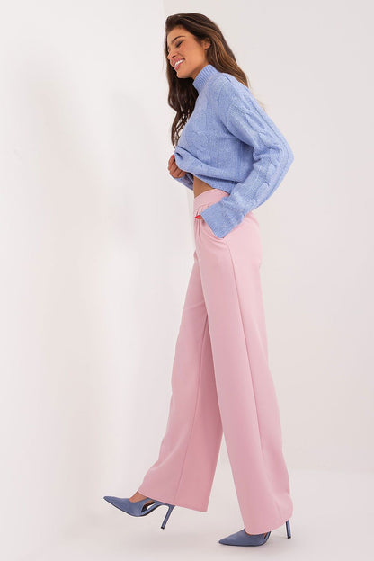 Side profile of an elegant woman wearing tailored pink trousers paired with a blue cropped sweater, exuding modern sophistication by Rue Paris.