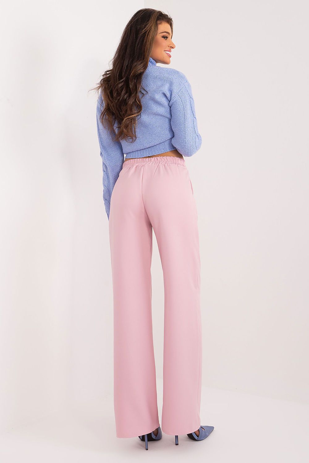 Back view of an elegant woman in high waist pink trousers and a blue cropped jumper, showcasing a chic and timeless style by Rue Paris.