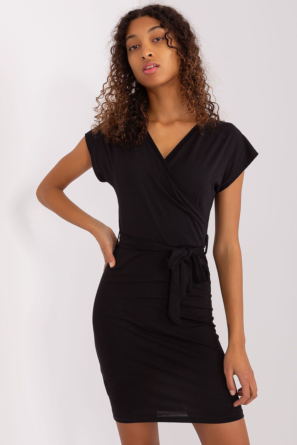 A woman poses confidently in a sophisticated black cotton summer pencil dress with a tie belt by Rue Paris, accentuating her waist in a luxurious setting.