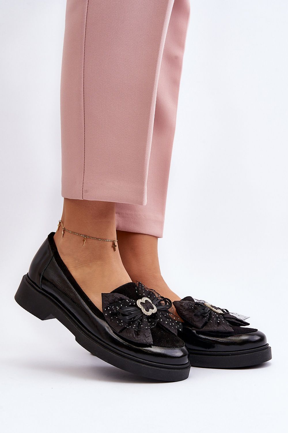 Elegant black leather moccasins from Step in Style, featuring a decorative bow and sparkling details, styled with tailored pink trousers for a chic spring look.