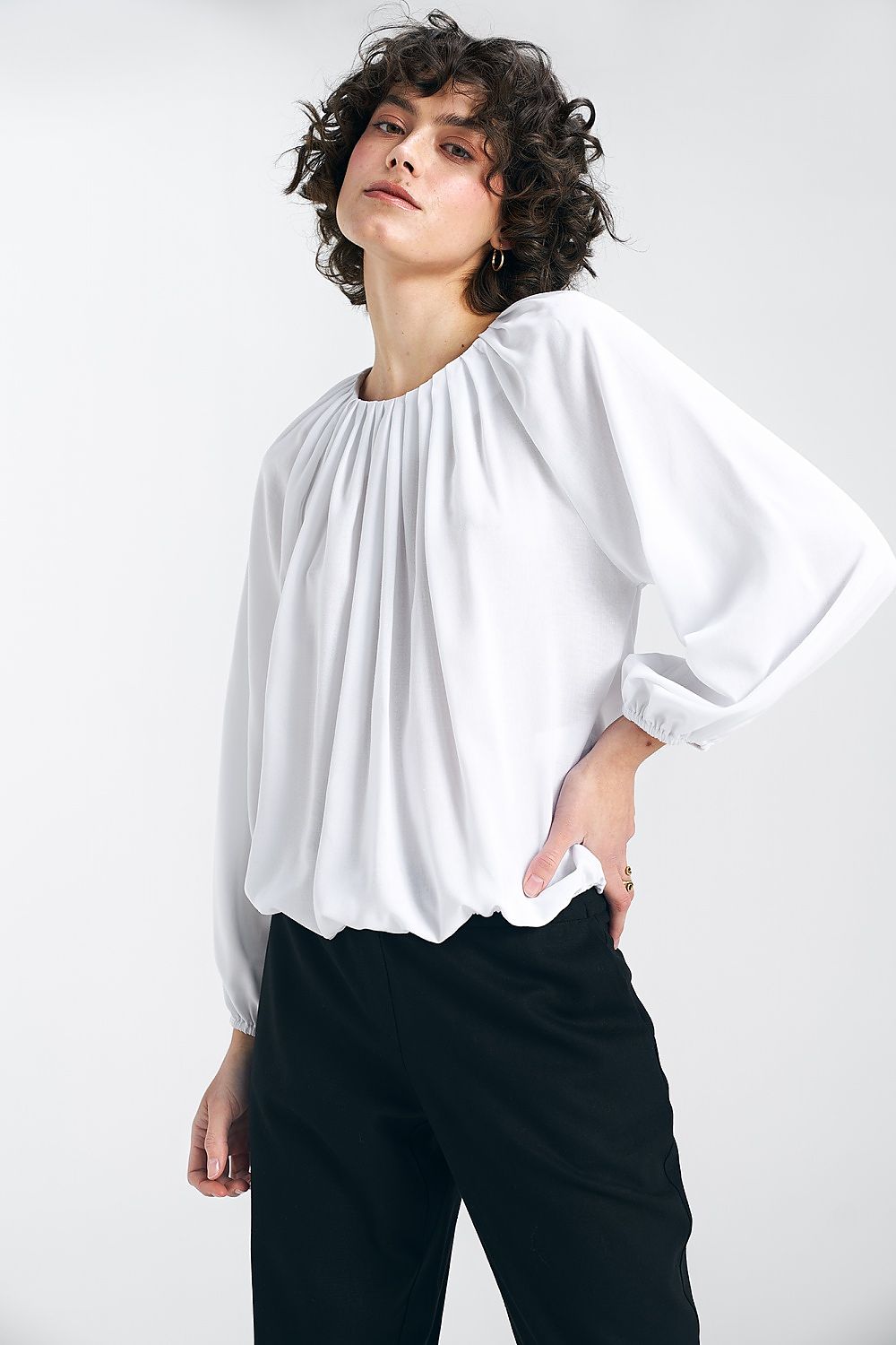 Side view of the white Nife viscose blouse, showcasing its fashionable pleats and casual elegance, paired with trousers for sophistication.