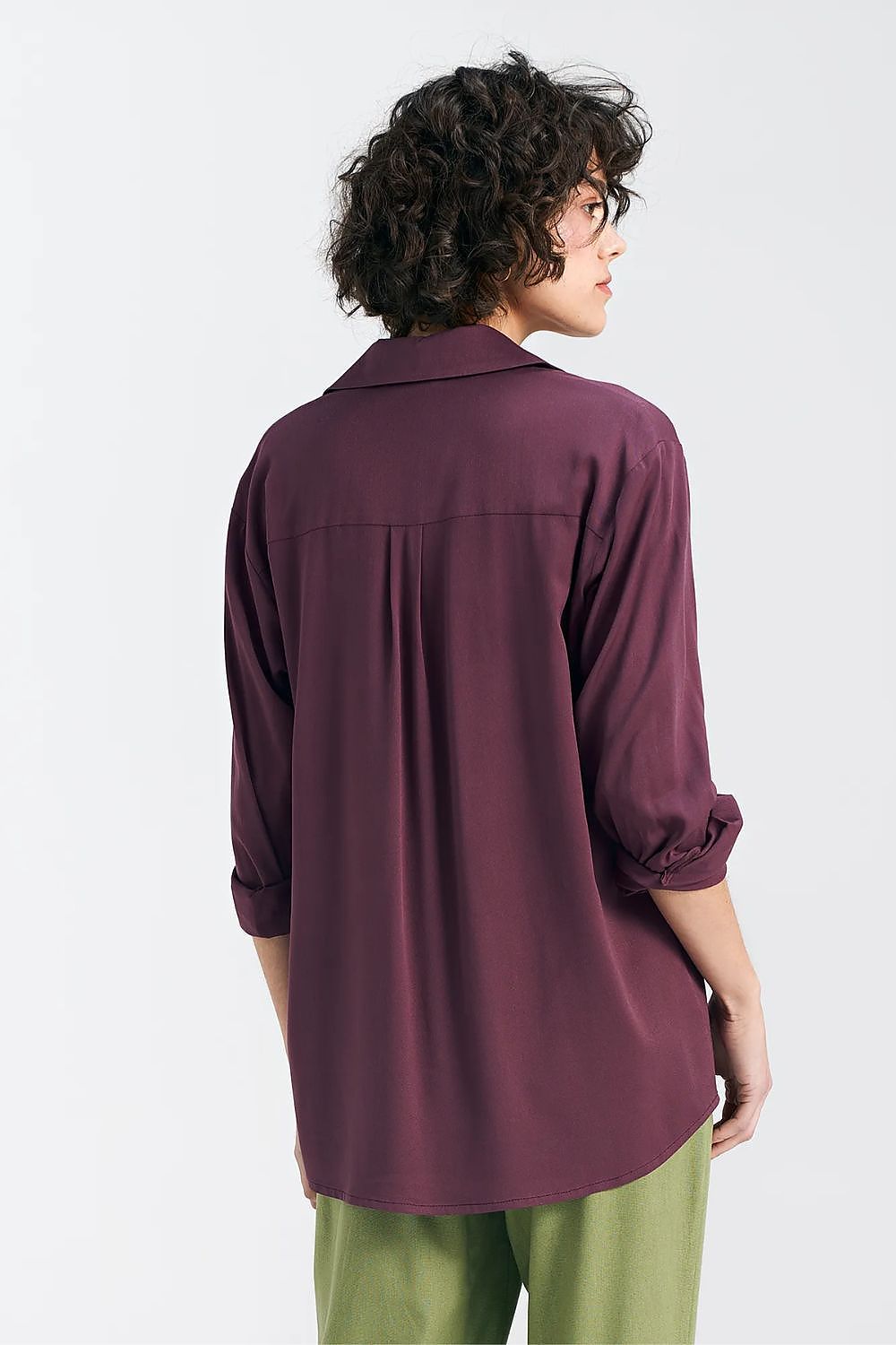 Back view of the elegant oversized long sleeve viscose shirt in deep plum by Nife, showcasing the flowing silhouette and yoke detail, styled with green tailored trousers.