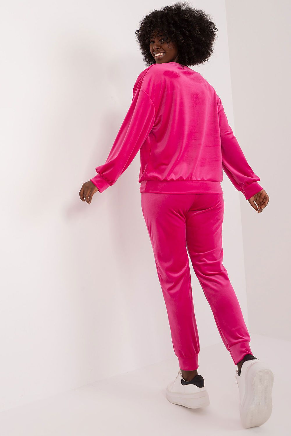 Stylish woman showcasing the back view of the Italy Moda Velour 2-Piece Sweatshirt and Pants Set in vibrant pink, featuring elegant drawstrings and bow detail.