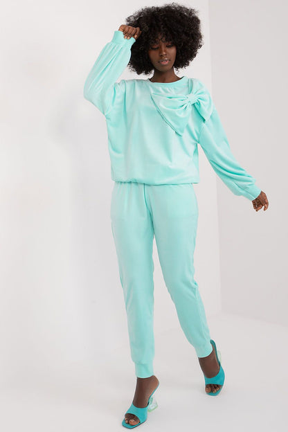 Chic woman wearing the Italy Moda Velour 2-Piece Sweatshirt and Pants Set in soft aqua, featuring an elegant bow detail on the blouse, ideal for a luxurious casual look.